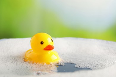 Photo of Cute rubber duck floating in water with bubbles against blurred green background, closeup