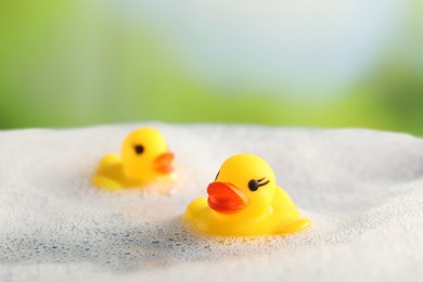 Photo of Cute rubber ducks floating in water with bubbles against blurred green background, closeup