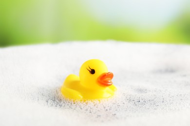 Photo of Cute rubber duck floating in water with bubbles against blurred green background, closeup