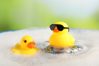 Photo of Cute rubber ducks floating in water with bubbles against blurred green background, closeup