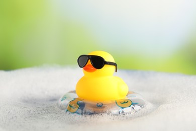 Photo of Cute rubber duck floating in water with bubbles against blurred green background, closeup