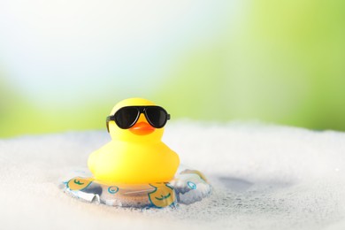 Photo of Cute rubber duck floating in water with bubbles against blurred green background, closeup