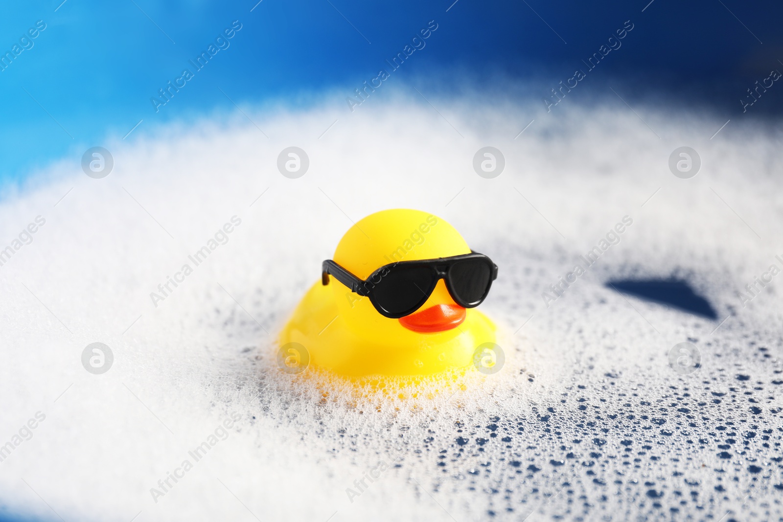 Cute rubber duck floating in water with bubbles against blue background, closeup Photo of Cute rubber duck floating in water with bubbles against blue background, closeup