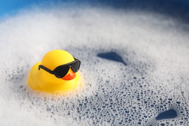 Photo of Cute rubber duck floating in water with bubbles against blue background, closeup