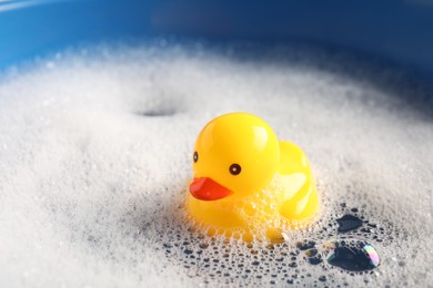 Photo of Cute rubber duck floating in water with bubbles against blue background, closeup