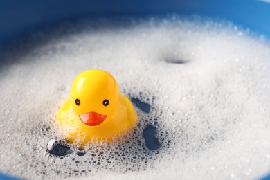 Photo of Cute rubber duck floating in water with bubbles against blue background, closeup