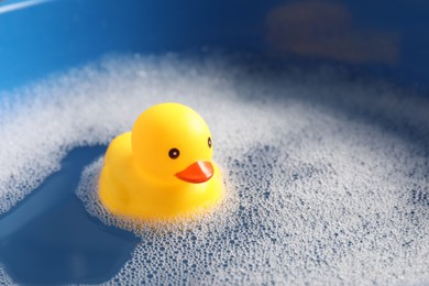 Photo of Cute rubber duck floating in water with bubbles, closeup