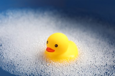 Photo of Cute rubber duck floating in water with bubbles, closeup