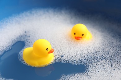 Photo of Cute rubber ducks floating in water with bubbles, closeup