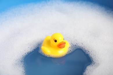 Photo of Cute rubber duck floating in water with bubbles, closeup