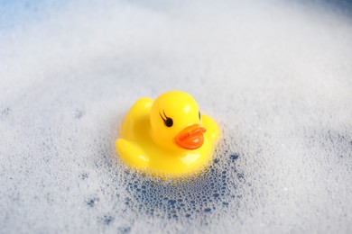 Photo of Cute rubber duck floating in water with foam, closeup