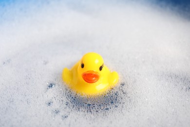 Photo of Cute rubber duck floating in water with foam, closeup