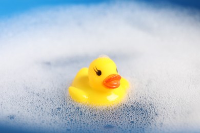 Photo of Cute rubber duck floating in water with bubbles, closeup