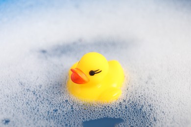Photo of Cute rubber duck floating in water with bubbles, closeup