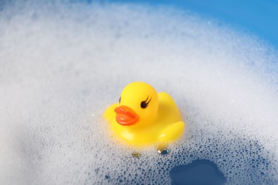 Photo of Cute rubber duck floating in water with bubbles, closeup