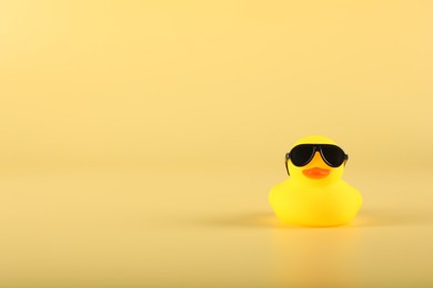 Photo of Cute rubber duck with sunglasses on yellow background, space for text