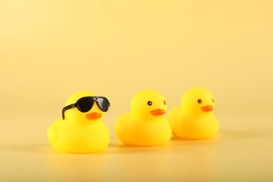 Photo of Three cute rubber ducks on yellow background, closeup