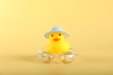 Photo of Cute rubber duck in hat and inflatable ring on yellow background