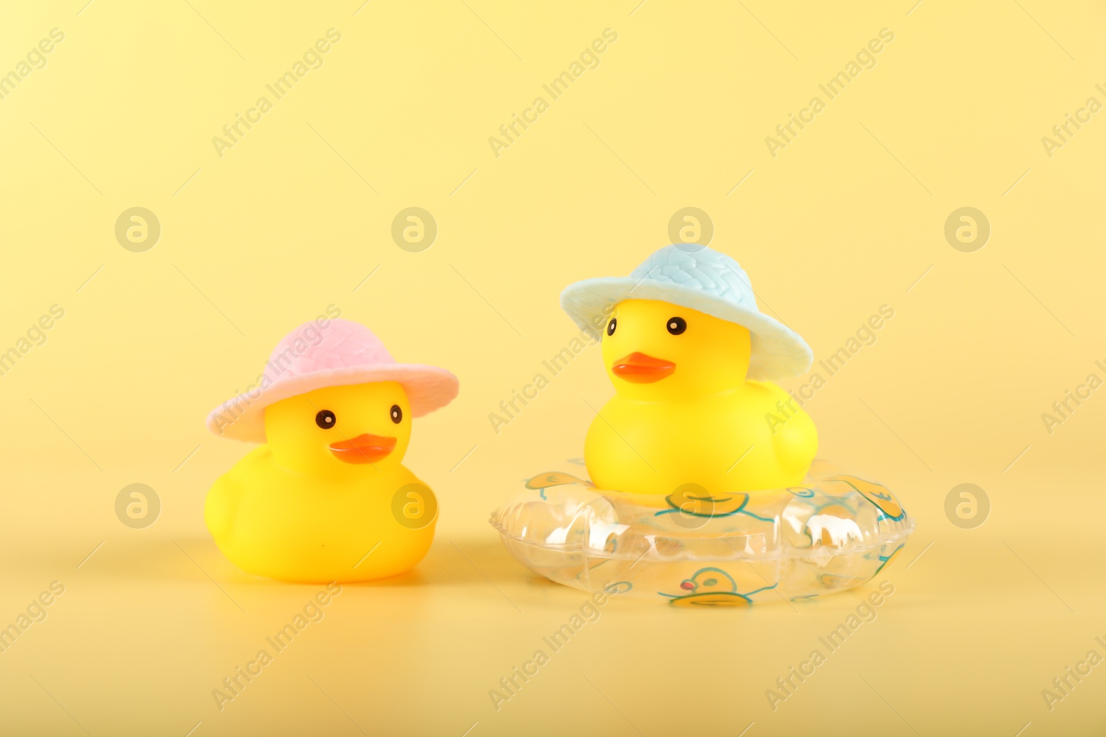 Cute rubber ducks in hats and inflatable ring on yellow background Photo of Cute rubber ducks in hats and inflatable ring on yellow background