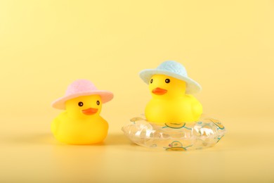 Photo of Cute rubber ducks in hats and inflatable ring on yellow background