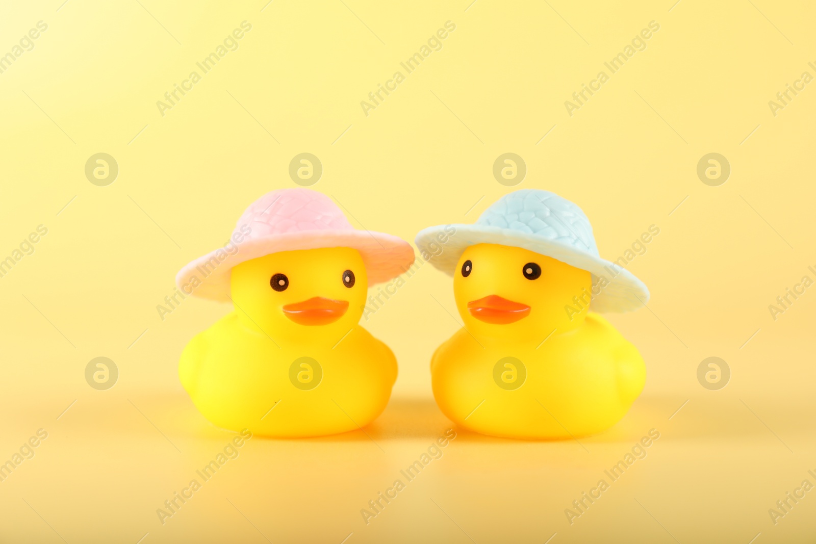 Cute rubber ducks in hats on yellow background Photo of Cute rubber ducks in hats on yellow background
