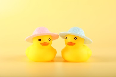 Photo of Cute rubber ducks in hats on yellow background