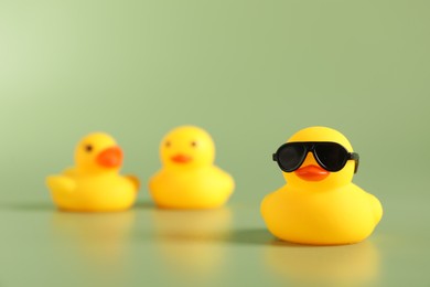 Photo of Three cute rubber ducks on green background, selective focus