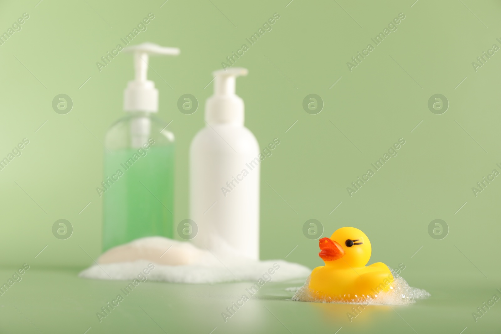 Cute rubber duck, foam, soap and bottles of cosmetic products on green background Photo of Cute rubber duck, foam, soap and bottles of cosmetic products on green background