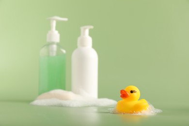 Photo of Cute rubber duck, foam, soap and bottles of cosmetic products on green background