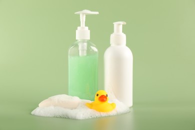 Photo of Cute rubber duck, foam, soap and bottles of cosmetic products on green background