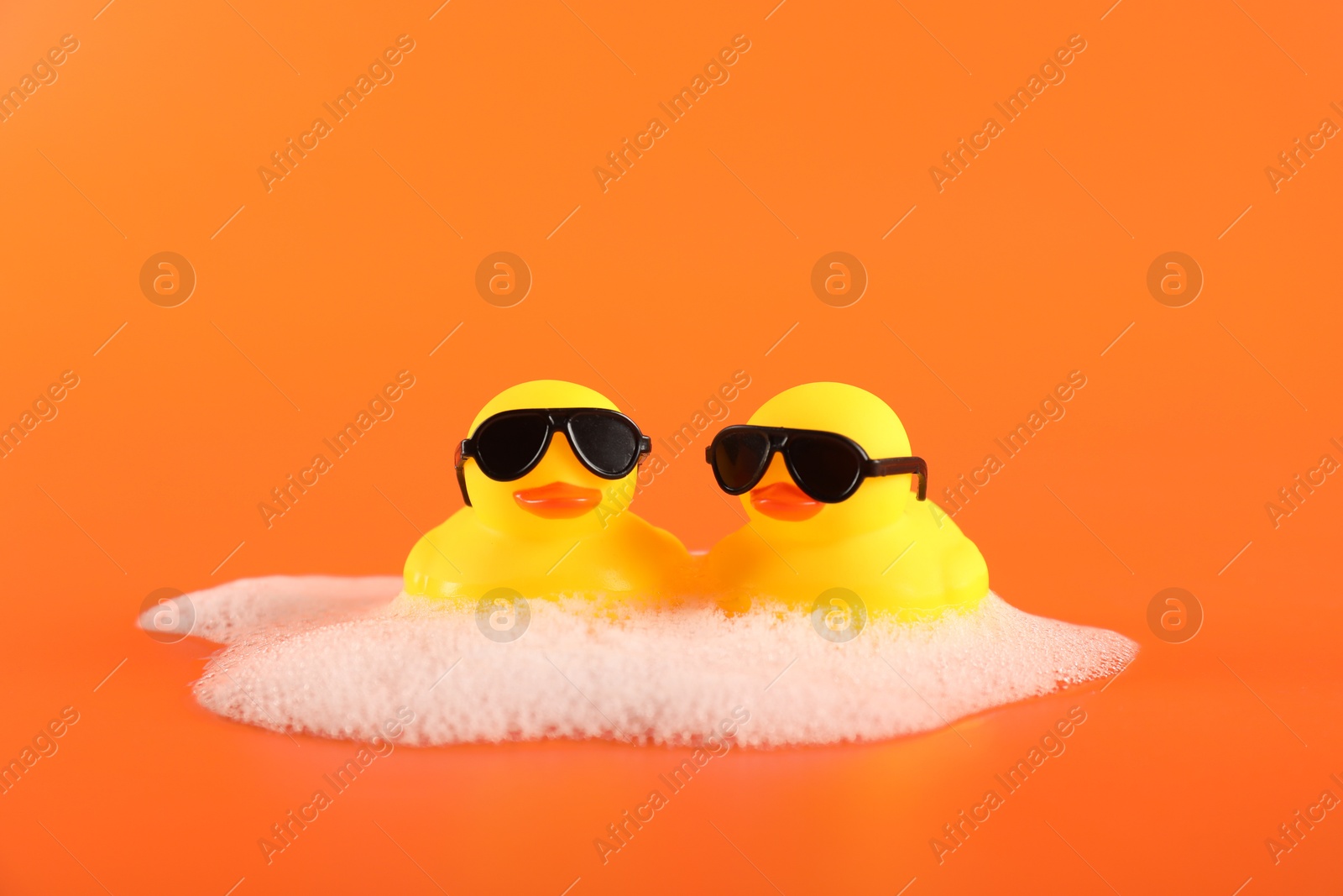 Cute rubber ducks with sunglasses and foam on orange background Photo of Cute rubber ducks with sunglasses and foam on orange background