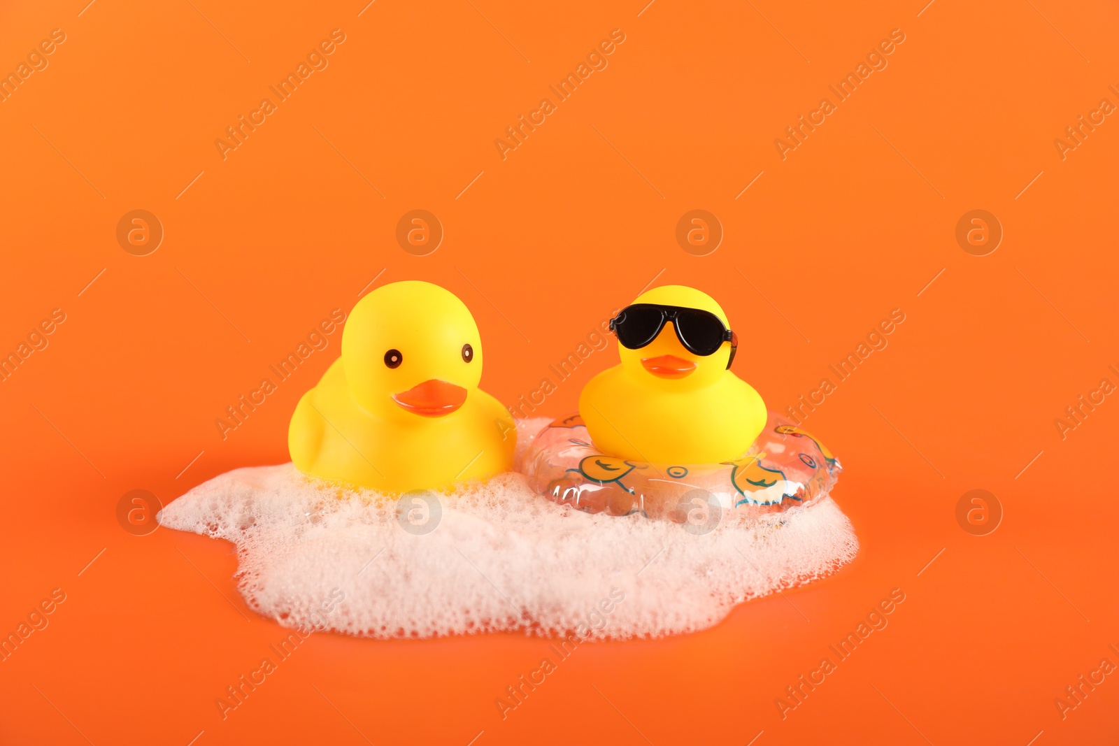 Cute rubber ducks, foam and inflatable ring on orange background Photo of Cute rubber ducks, foam and inflatable ring on orange background