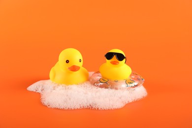 Photo of Cute rubber ducks, foam and inflatable ring on orange background