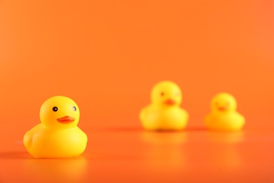 Photo of Three cute rubber ducks on orange background, selective focus. Space for text
