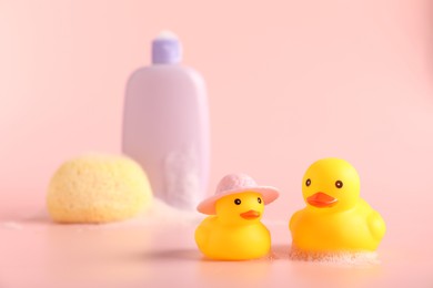Photo of Cute rubber ducks, sponge and bottle of shampoo on pink background