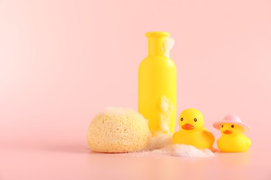 Photo of Cute rubber ducks, sponge and bottle of shampoo on pink background, space for text