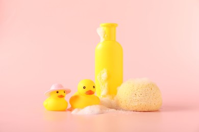 Photo of Cute rubber ducks, sponge and bottle of shampoo on pink background