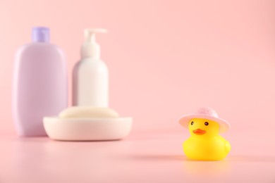 Photo of Cute rubber duck in hat, soap and bottles of cosmetic products on pink background
