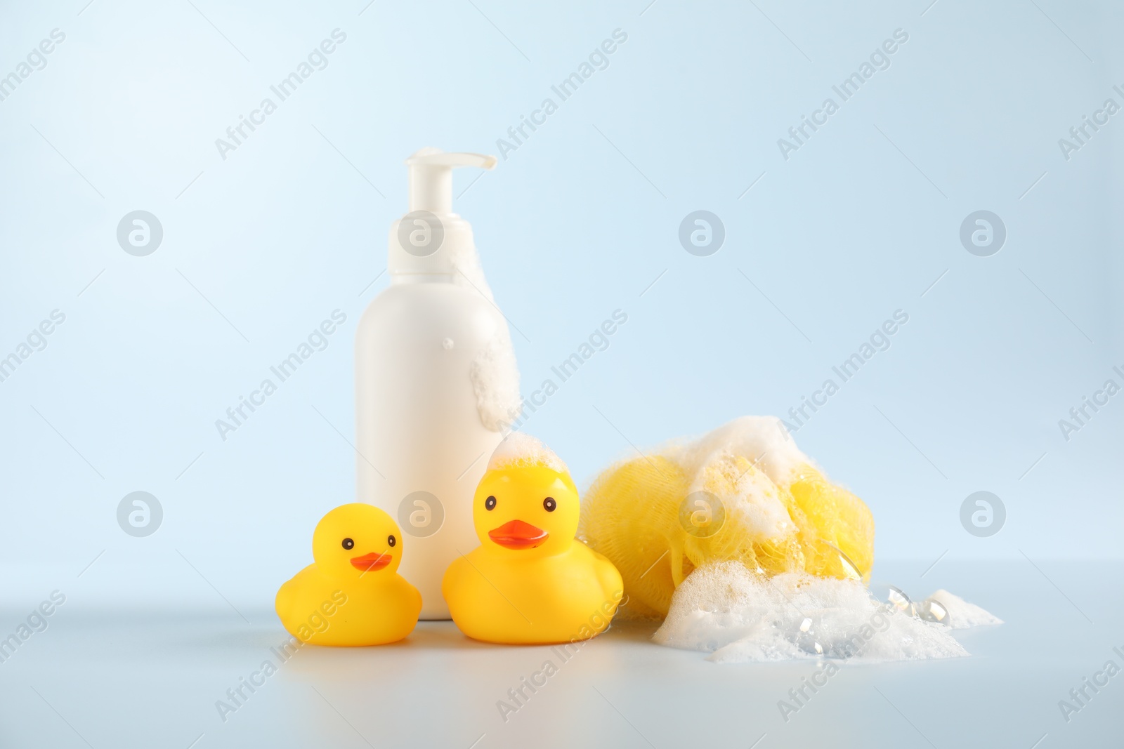 Cute rubber ducks, sponge and bottle of cosmetic product on white background Photo of Cute rubber ducks, sponge and bottle of cosmetic product on white background