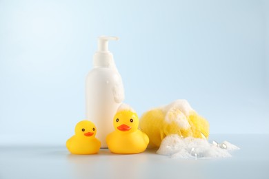 Photo of Cute rubber ducks, sponge and bottle of cosmetic product on white background