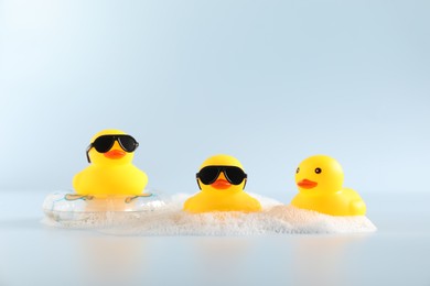 Photo of Three cute rubber ducks, foam and inflatable ring on white background