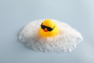 Photo of Cute rubber duck in sunglasses and foam on white background, closeup