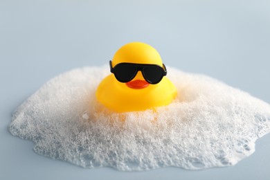Photo of Cute rubber duck in sunglasses and foam on white background, closeup