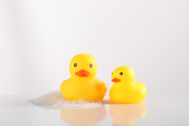 Photo of Cute rubber ducks and foam on white background