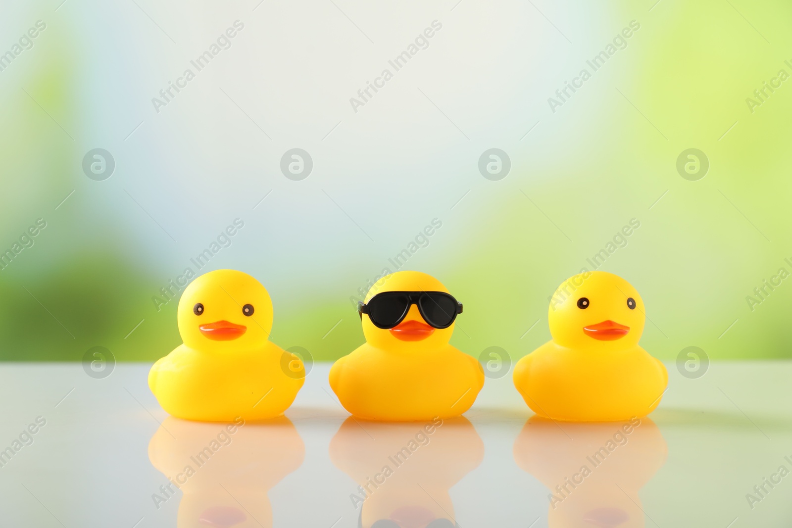 Three cute rubber ducks on table against blurred background Photo of Three cute rubber ducks on table against blurred background