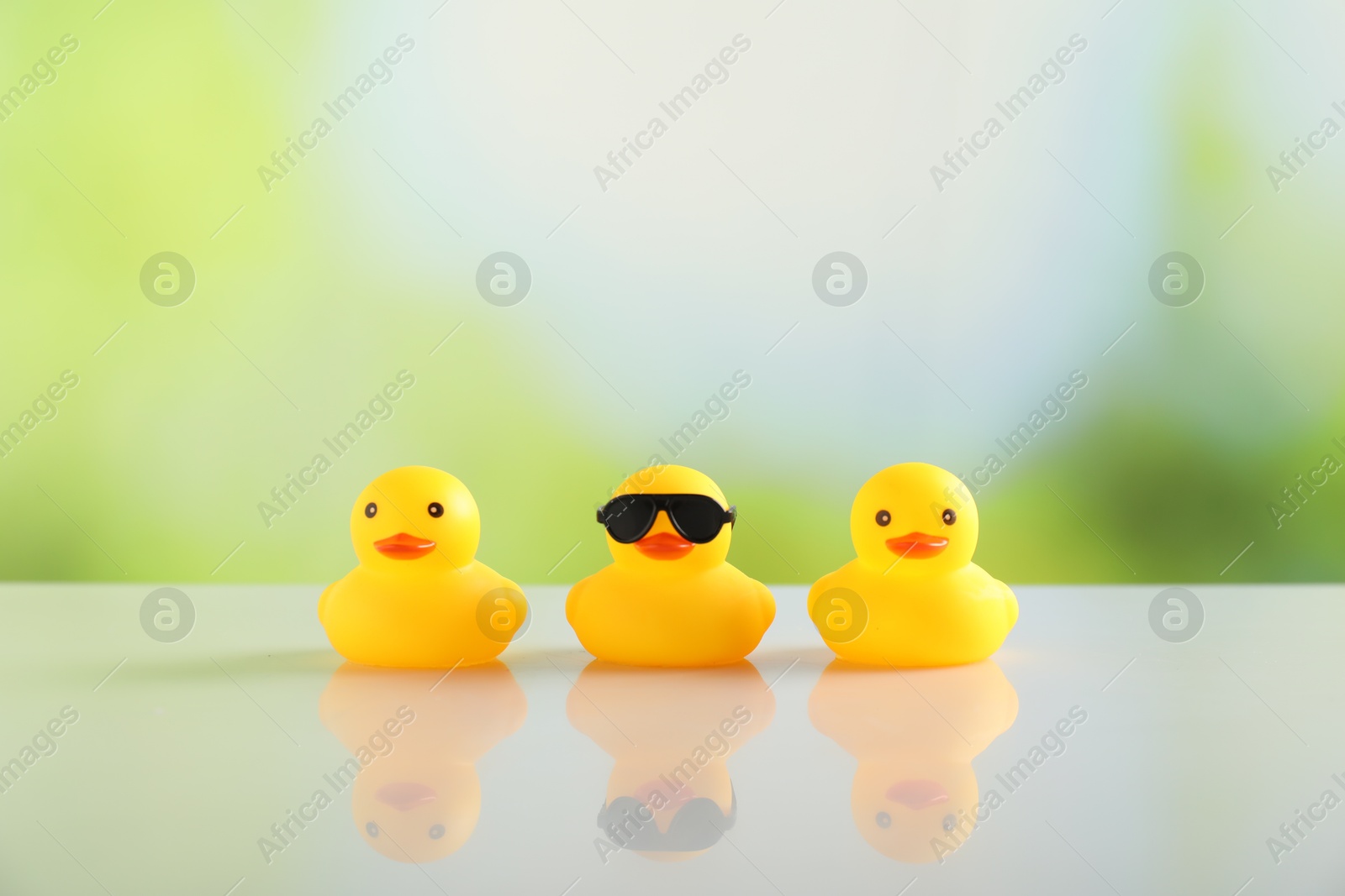 Three cute rubber ducks on table against blurred background Photo of Three cute rubber ducks on table against blurred background