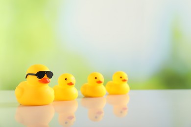 Photo of Cute rubber ducks on table against blurred background, closeup. Space for text