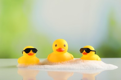 Photo of Cute rubber ducks and foam on table against blurred background, closeup