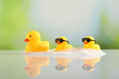 Photo of Cute rubber ducks and foam on table against blurred background