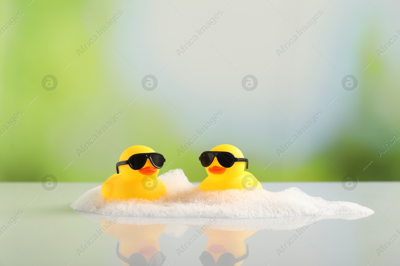 Cute rubber ducks and foam on table against blurred background Photo of Cute rubber ducks and foam on table against blurred background